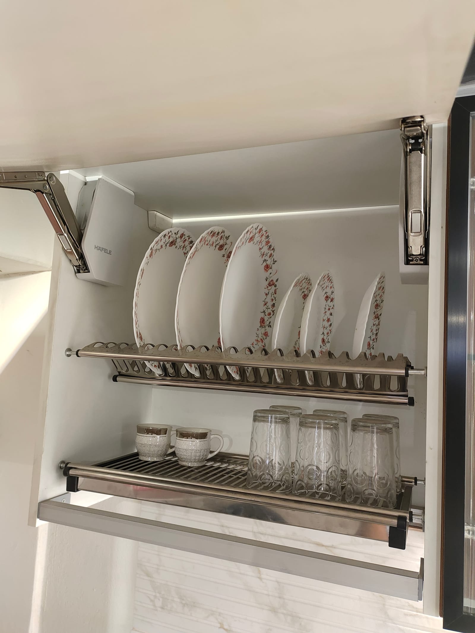 An open wall unit holding a stainless steel plate rack above a tray sized for glasses and cups