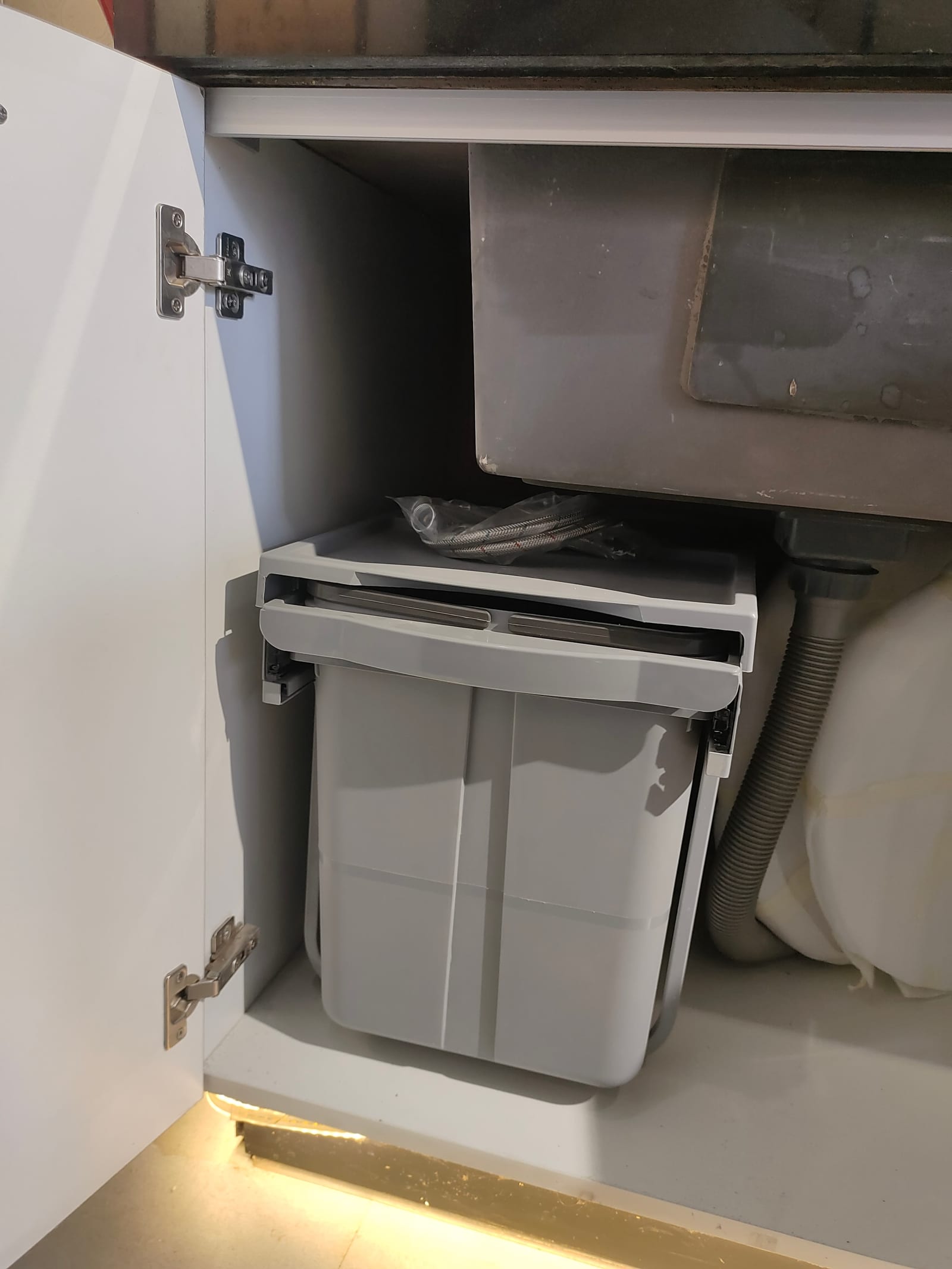 A bin mounted inside a sink base unit so that it slides out when the door is opened