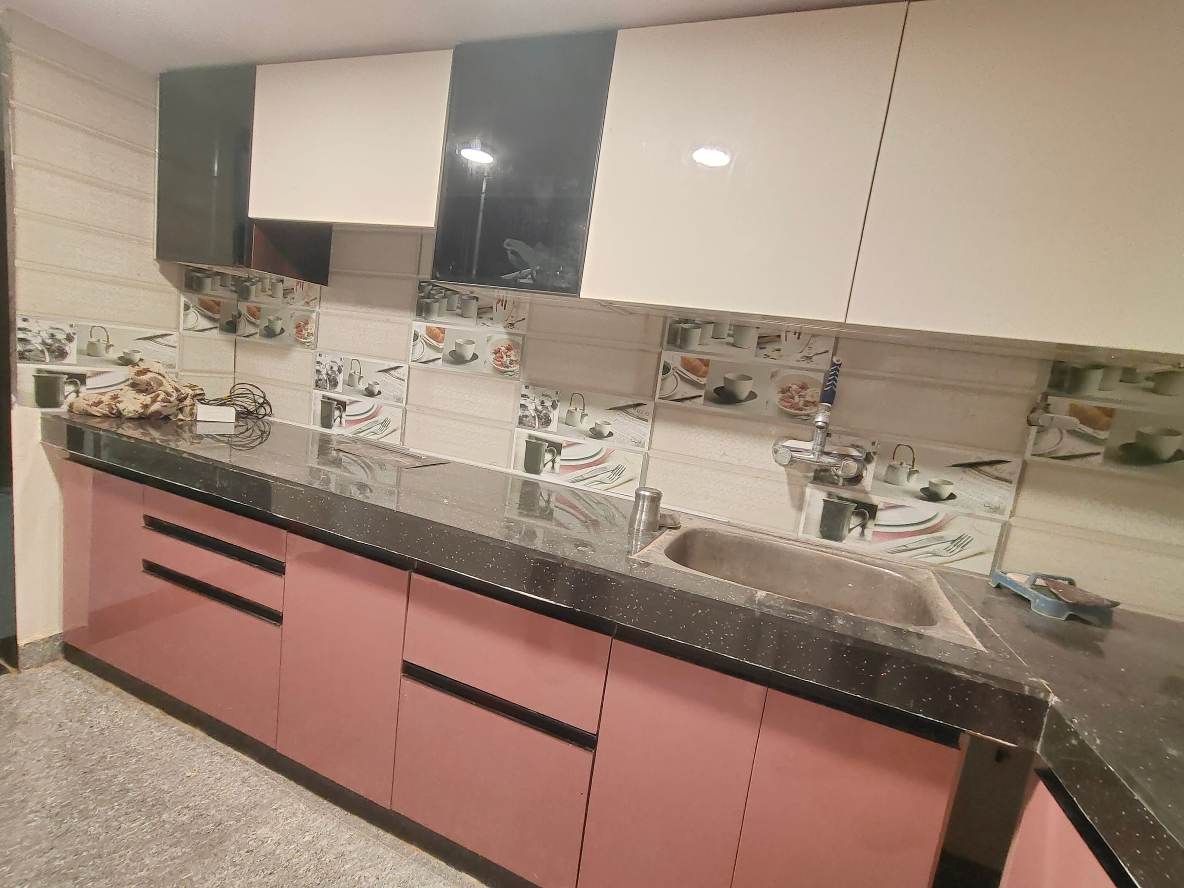 The same kitchen as built, photographed on handover day, with the rose base units and granite counter in place under white and black gloss wall cabinets
